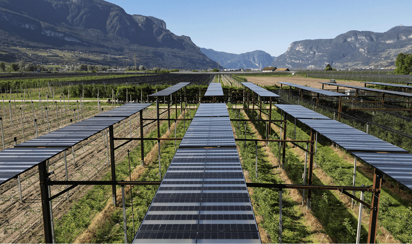Solar panels above farmland, with mountains in the background. In Bolzano, Italy.